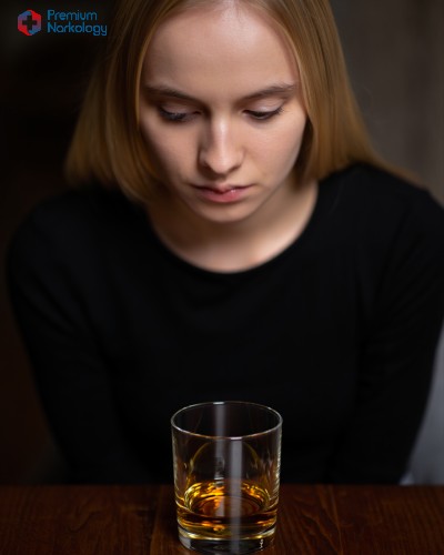 Женщина удрученно смотрит на стакан с алкоголем