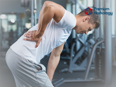 Мужчина на тренировке в спортзале держится за спину